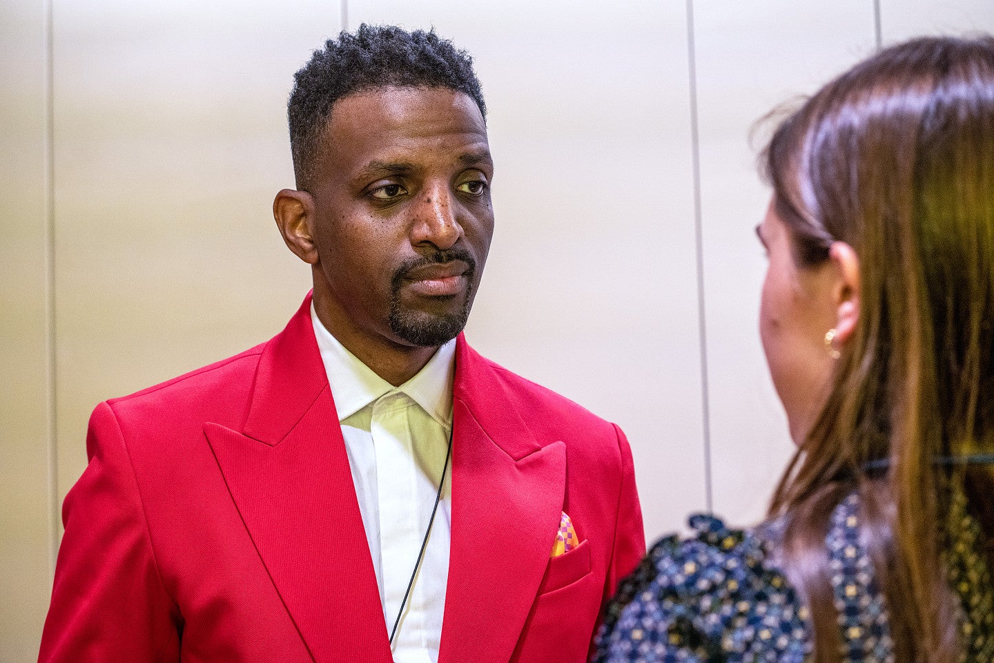 J. Ivy, wearing a bright red suit jacket, being interviewed by a student