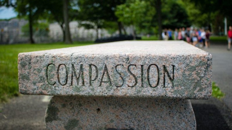 A stone bench in a public park with the word compassion engraved on the side