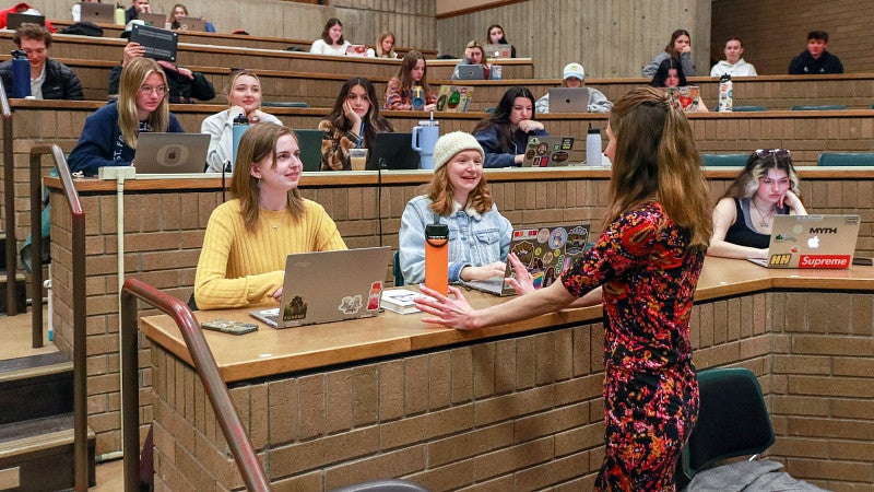 Whitney Phillips speaks to two students in a large classroom