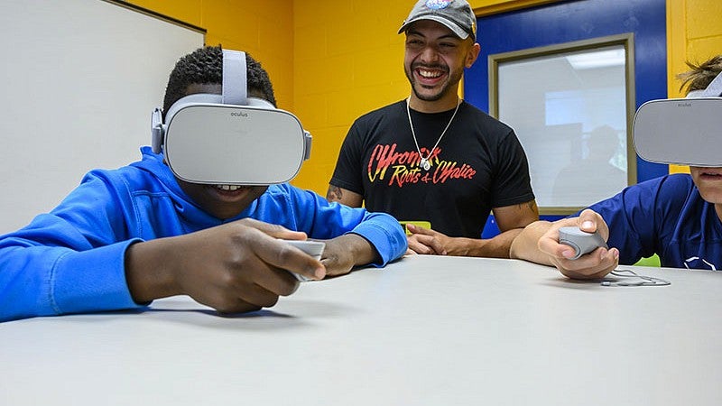 Two people play with virtual reality devices while an instructor watches.