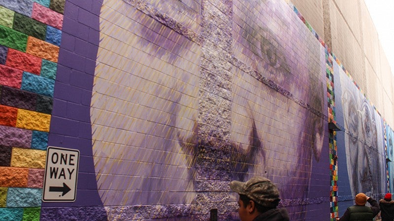 A person wearing a camouflage hat takes a photo of a purple mural.
