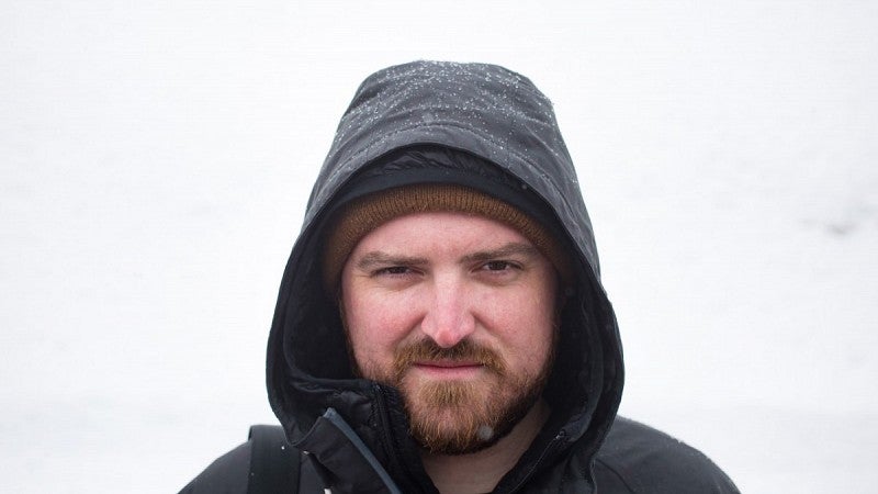 Jeff Dean looks into the lens while wearing a dark hooded rain jacket.