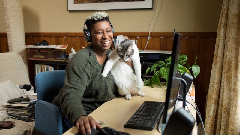 Tiara Darnell laughs at her computer while petting her cat.