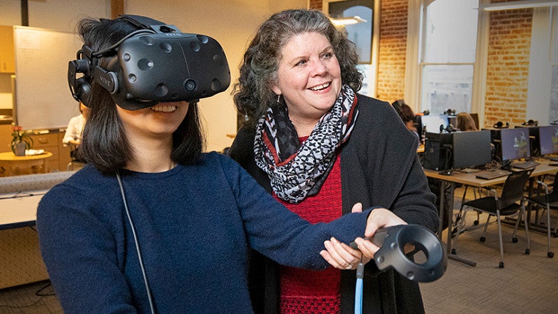 female student using wearable VR technology, assisted by female professor