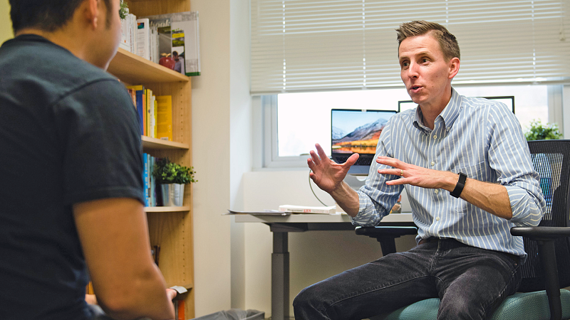 Seth Lewis gestures to a student while seated in his office