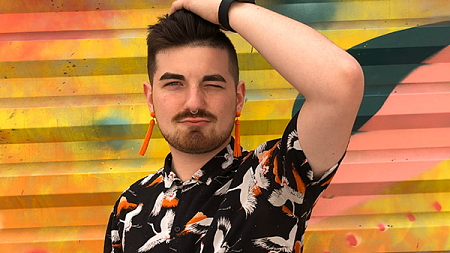 student wearing colorful shirt and earrings, posing in front of colorful mural