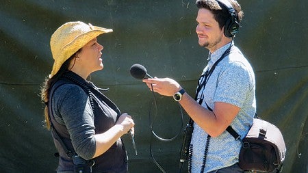 A male student with recording equipment interviewing a woman wearing a cowboy hat