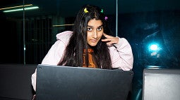 A young woman with colorful hair clips at her computer.