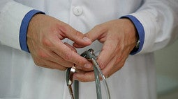 A doctor's hands, holding a stethoscope, are shown.
