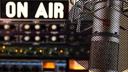 Image of a radio station's mic and audio controls, with a lighted "on air" sign in back.