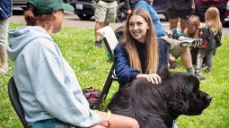 Alexis Weisend pets a large black dog while talking to its owner