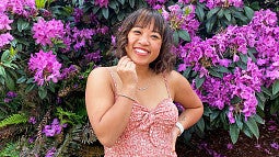 Kayla Nguyen stands in front of a flowering purple rhodedendron
