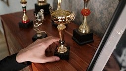 A hand reaching toward several trophies sitting on a dresser.