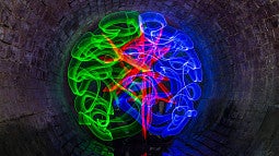 Bright swirls of green, red and blue come together to form the image of a human brain. 
