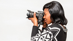 A black female photographer holds up a camera to her eye to take a photo (By Charles Wundengba from Pexels).