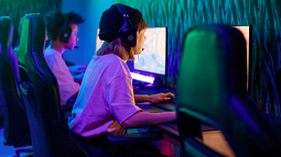 A woman sits in front of a computer monitor while wearing a gaming headset. 