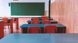 An empty classroom with wood paneling and blue desks (By Dids from Pexels).