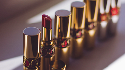 Several lipsticks, including one opened tube, are lined up on a sunny windowsill (By Valeria Boltneva from Pexels).