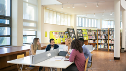 A group of college students sit together in a library working on a project (By Kampus Production from Pexels).