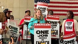 Liz Schuler, AFL-CIO president, stands at a podium surrounded by supporters and backed by the US flag