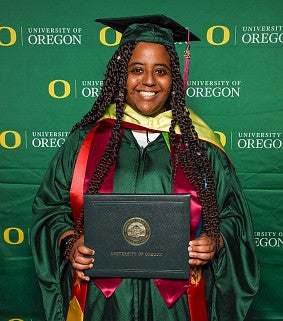 Yordanos Tesfazion poses with her diploma while wearing a green commencement cap and gown