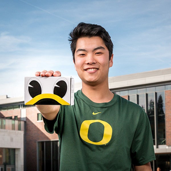 Travis Kim holds a UO360 cardboard viewfinder featuring the eyes and bill of the UO Duck mascot