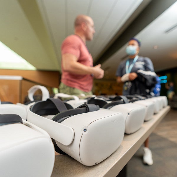 VR headsets lined up on a table in the foreground with two people talking in the background